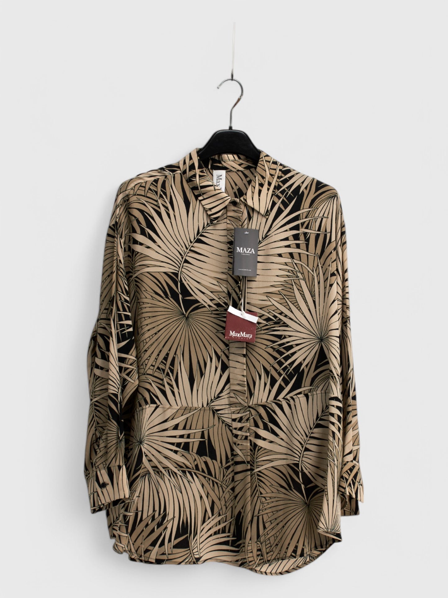Beige silk blouse with brown leaf pattern, long sleeves and collar, hanging on a hanger against a white background